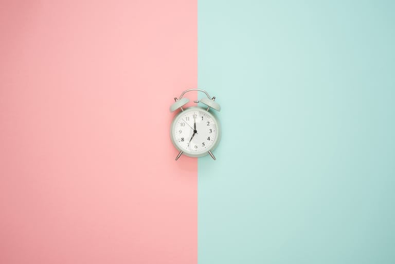 A vintage round clock on a split pastel pink and blue background.