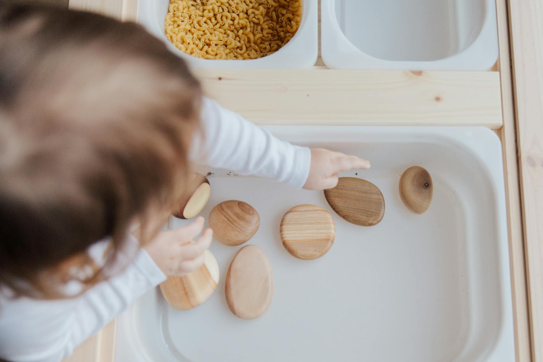 crop anonymous child getting brown stones from white container at home