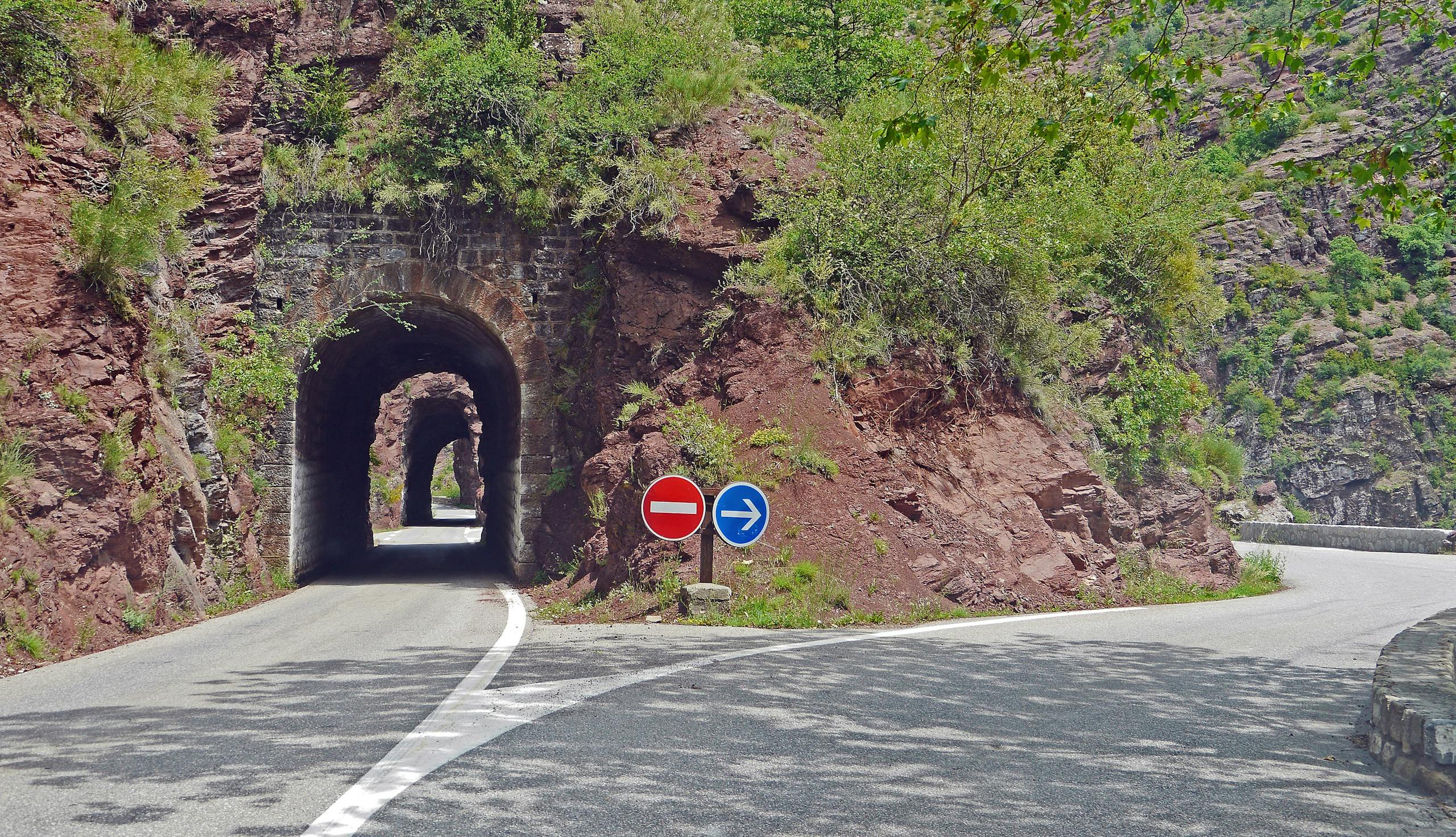 Picturesque mountain road with tunnel and directional signs on a sunny day.